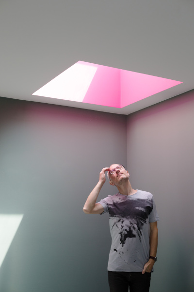 Johannes Hartl schaut nach oben und sieht in eine Öffnung in der Decke, in die Licht hereinfällt, das einen roafarbenen Kegel wirft.