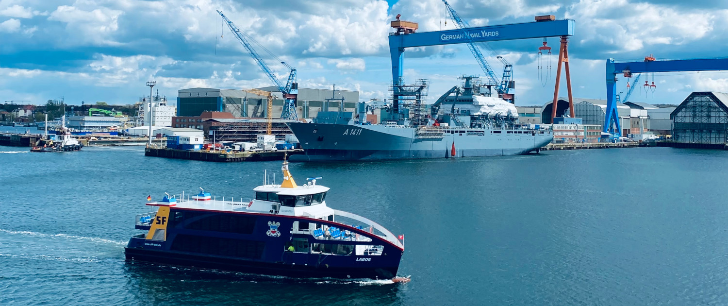 opener_kiel_1500 Blick auf die Kieler Förde, im Hintergrund ist die Werft zu sehen, im Vordergrund eine kleine Hafenfähre.