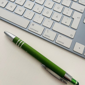 Blick auf einen modernen Schreibtisch, im Hintergrund eine Tastatur, im Vordergrund ein Kugelschreiber.